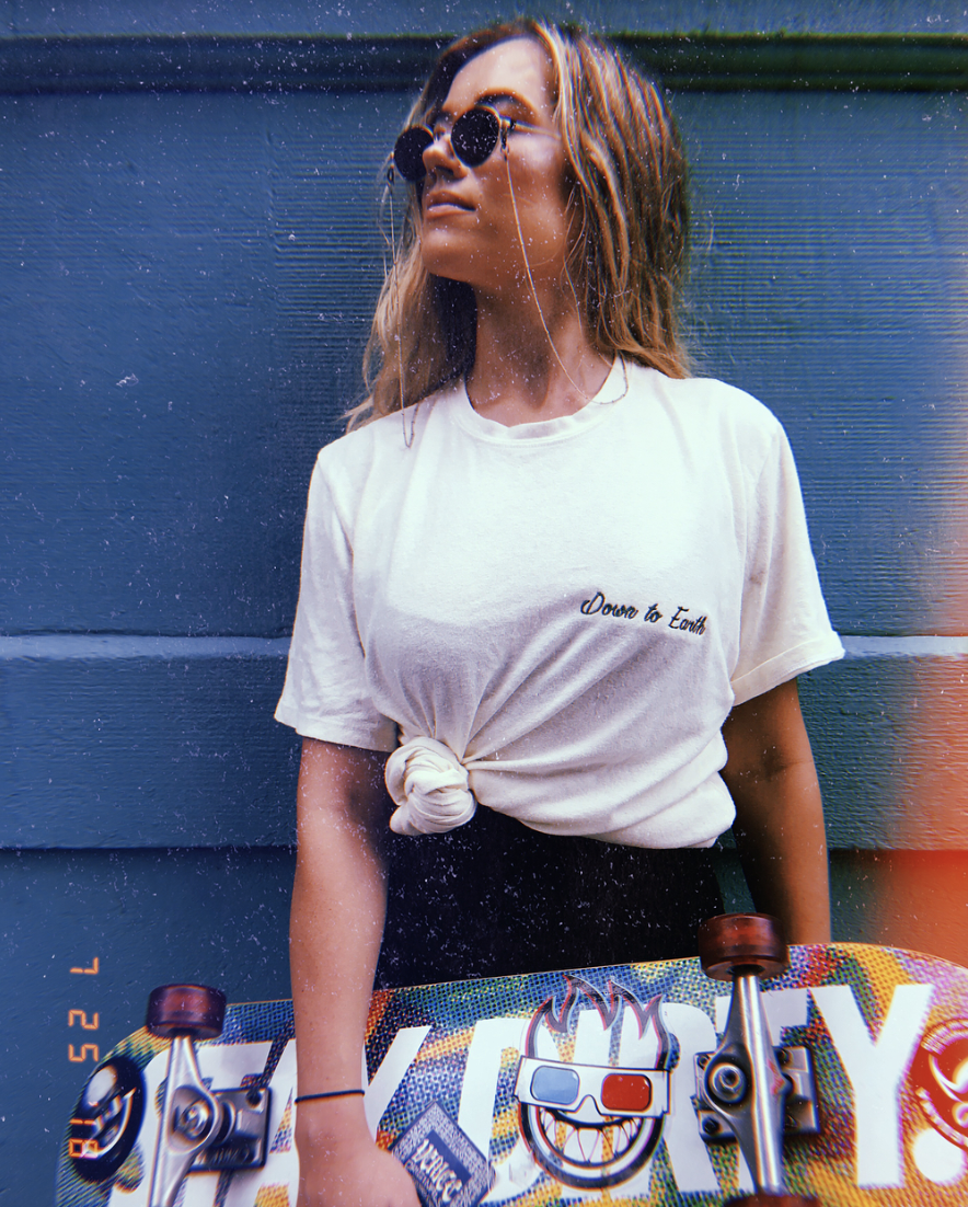 Lucy McBride, owner of Hood Hippie Vintage, posing with a skateboard and stylish outfit featuring a t-shirt from Down to Earth Original.