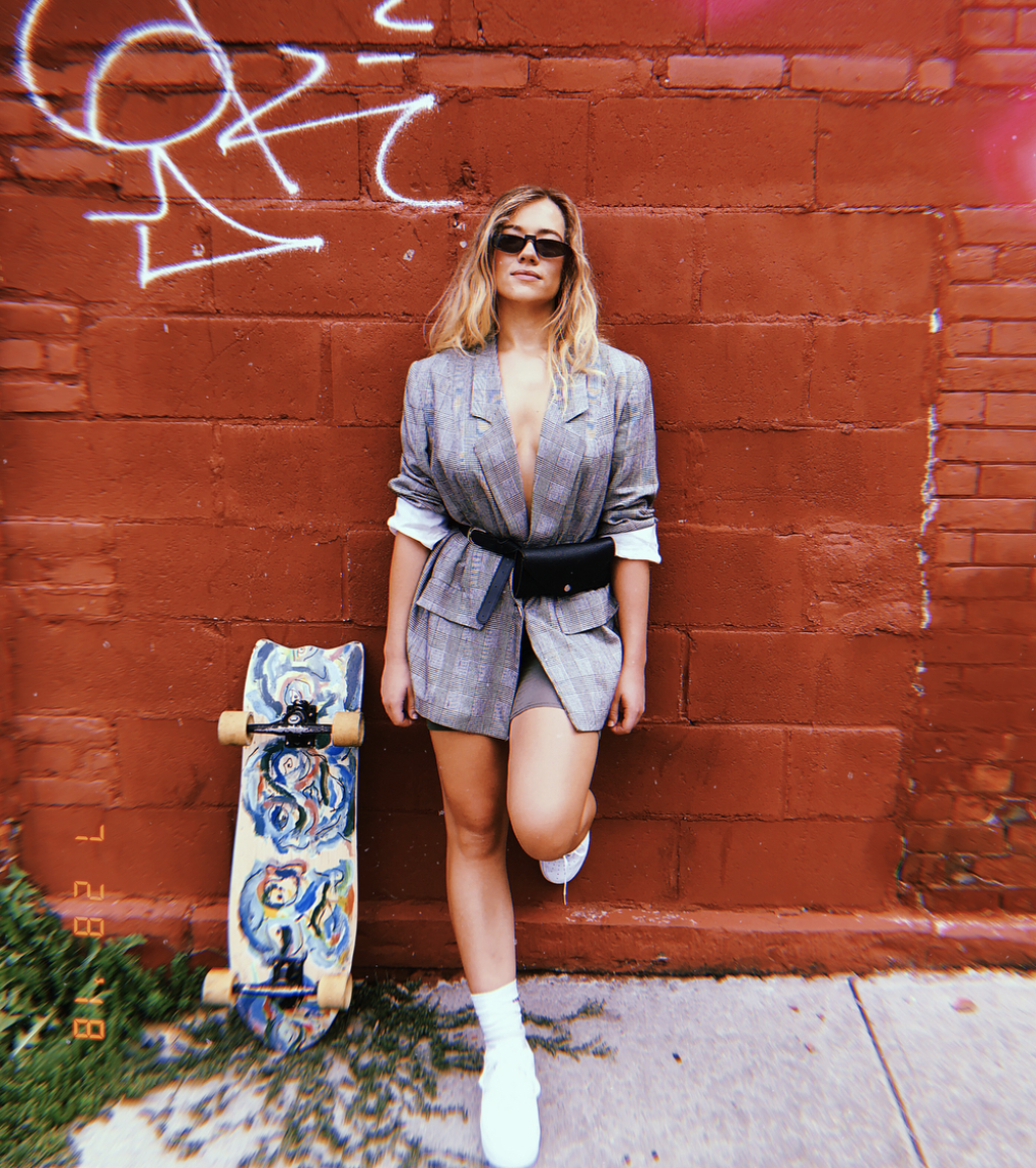 Lucy McBride founder of Hood Hippie Vintage poses in an 1980s vintage outfit consisting of a plaid blazer, bike shorts, and sneakers.